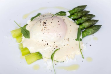 Yeşil kuşkonmaz, ve haşlanmış yumurta, hollandaise sosu, beyaz bir tabakta, yakın, izole. Buharda pişmiş yumurta ve kuşkonmaz.