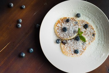 Yuvarlak bir tabakta krep, yukarıdan çilek ve şeker tozu. Masada krep, böğürtlen ve şeker tozu tabağı.