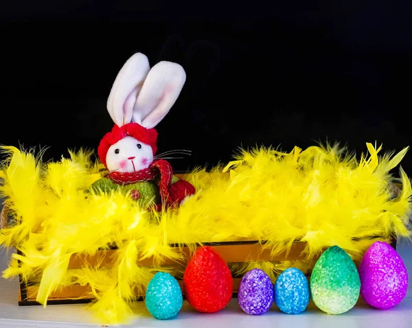 Easter bunny, coloful eggs and yellow feathers on black background.