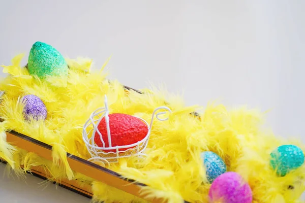 Пасхальные цветные яйца и желтые перья в корзине — стоковое фото