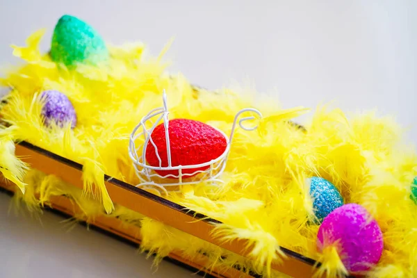 Пасхальные цветные яйца и желтые перья в корзине — стоковое фото