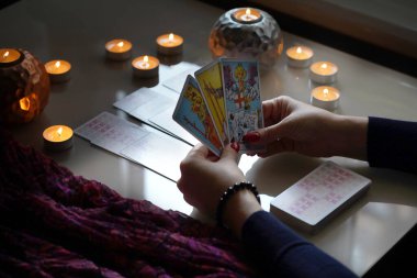 Tarot okuyucusu yanan mumların yanında tarot kartları topluyor..