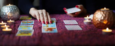 Tarot okuyucusu yanan mumların yanında tarot kartları topluyor..