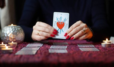 Tarot okuyucusu yanan mumların yanında tarot kartları topluyor..