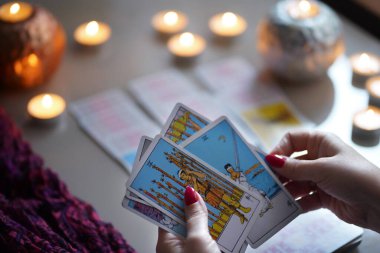 Tarot okuyucusu yanan mumların yanında tarot kartları topluyor..