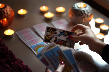 Tarot okuyucusu yanan mumların yanında tarot kartları topluyor..