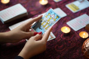 Tarot okuyucusu yanan mumların yanında tarot kartları topluyor..
