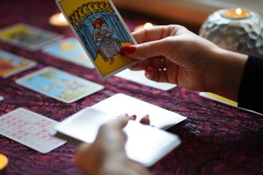 Tarot okuyucusu yanan mumların yanında tarot kartları topluyor..