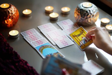 Tarot okuyucusu yanan mumların yanında tarot kartları topluyor..