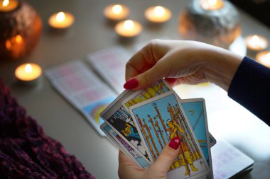 Tarot okuyucusu yanan mumların yanında tarot kartları topluyor..