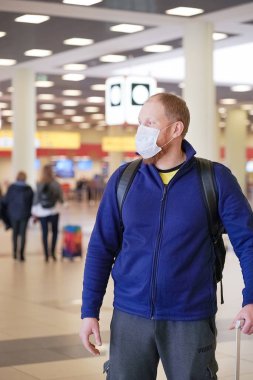 Avrupalı kızıl sakallı adam havaalanında koruyucu tıbbi maske takıyor.