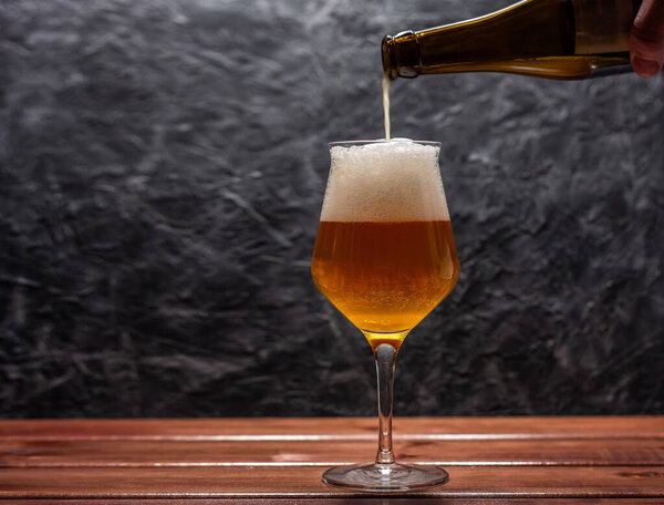 A pint of light beer is poured into a glass of Belgian form from a bottle on a wall in grunge or loft style