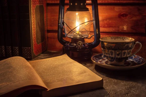 テーブルの上の暗い部屋で 古い手持ちの灯油ランプの光の中で本を読むことは静かに光る ヴィンテージスタイル 暗闇の中の光 ロフトスタイルの雰囲気の写真 — ストック写真