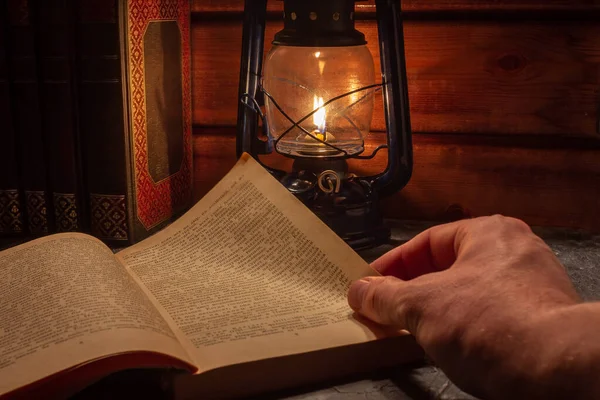 Reading a book in the light of an old hand-held kerosene lamp glows softly in a dark room on the table. Vintage style. The light in the darkness. Atmospheric photo in the loft style.