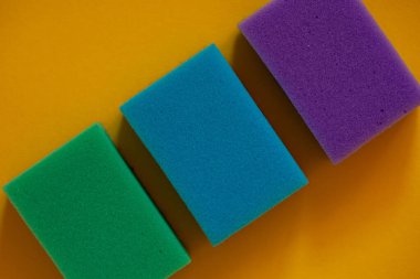 Temizlik ve yıkama kavramı. Sarı arka planda temizlik için renkli süngerlerin karışımı.