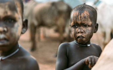 MUNDARI TRIBE, Güney Sudan, Afrika 'daki Mundari Kabile Köyü' nün otlağında arkadaşlarıyla çalışırken yüzünde çamur olan bir çocuk başka tarafa bakıyor.