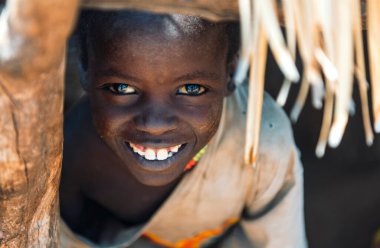 BOYA TRIBE, Güney SUDAN - 10 Mart 2020: Yansımalı güzel kahverengi gözlü iyimser çocuk pencere deliğinden dışarı bakıyor ve güneydeki köyde saklanırken kameraya gülümsüyor