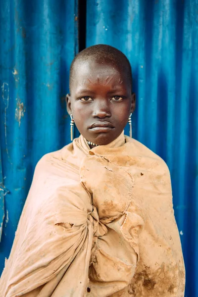 TOPOSA TRIBE, SOUTH SUDAN - MARCH 12, 2020: Teen girl looking at camera while standing against blue building wall in village of Toposa Tribe in South Sudan, Africa — Stock Photo, Image