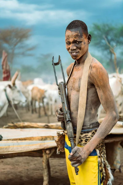 MUNDARI TRIBE, SUDÁN DEL SUR - 11 DE MARZO DE 2020: Joven con un arma de fuego sonriendo y mirando a la cámara mientras cuida el ganado de pastoreo de la tribu Mundari en Sudán del Sur, África — Foto de Stock