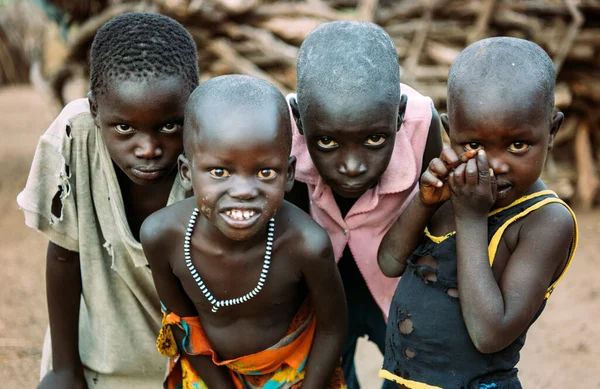 TOPOSA TRIBE, SOUTH SUDAN - MARCH 12, 2020: Anak laki-laki dalam pakaian kotor compang-camping melihat kamera pada latar belakang kabur Toposa Desa Suku di Sudan Selatan, Afrika — Stok Foto