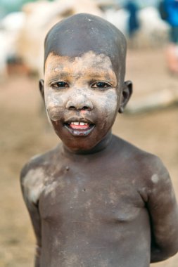 MUNDARI TRIBE, Güney Sudan - 11 Mart 2020: Geleneksel kül maskeli çocuk Güney Sudan 'da bulanık arka planda dururken kameraya ilgiyle bakıyor