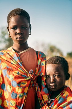 BOYA TRIBE, Güney SUDAN - 10 Mart 2020: Boya Kabilesi 'nden çocuklar parlak kumaş parçaları giyip güneşli Güney Sudan' da güneşli bir günde savananın bulanık arka planında dururken kameraya bakıyorlar