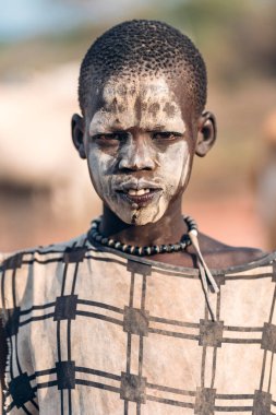 MUNDARI TRIBE, Güney Sudan, Afrika 'da Mundari Kabile Köyü' nde yaşarken geleneksel giysileri ve yüzleri çamurla boyanmış bir genç.