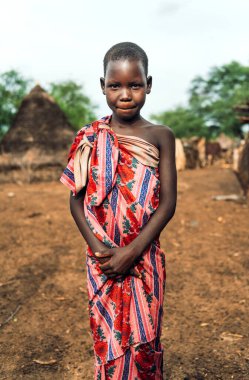 TOPOSA TRIBE, GÜNEY SUDAN - 12 Mart 2020: Güney Sudan, Afrika 'daki Toposa Kabile Köyü' nde yaşarken çiçek kumaşı ve kameraya sarılmış ve gülümseyen kız