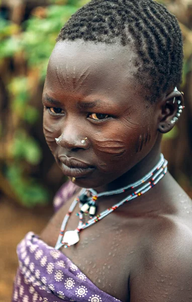 TOPOSA TRIBE, SOUTH SUDAN - 12 marca 2020: Nastolatka z bliznami na twarzy i tradycyjnymi akcesoriami odwracającymi wzrok, mieszkająca w miejscowości Toposa Tribe w Sudanie Południowym, Afryka — Zdjęcie stockowe
