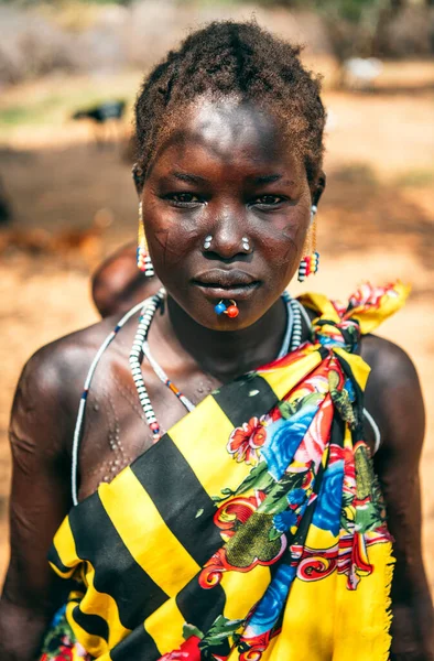 BOYA TRIBE, SOUTH SUDAN - 10 marca 2020: Kobieta w tradycyjnych kolorowych ubraniach i akcesoriach z rytualnymi kolczykami i modyfikacjami blizn patrząca przed kamerą w osadzie plemienia w Sudanie Południowym — Zdjęcie stockowe