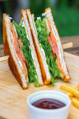 Somonlu sandviç, salata, sebze, marul, domates, soğan ve ahşap zemin üzerinde taze dilimlenmiş ekmek. Dikey fotoğraf. Kapat.