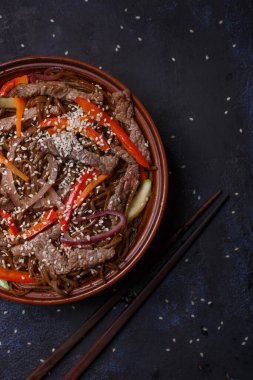 Tayland soslu domuz eti ve funcho noodle. Dikey fotoğraf. Japon yemeği. Siyah arka plan. Kahverengi kase. Alçak tuş