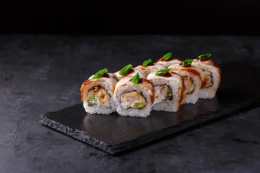 Suşi, yılan balığı, salatalık, nori, krema peyniri, soğan tüyü, soğan tüyü, karides susamı ve siyah zemin üzerine teriyaki soslu. Yatay fotoğraf. Japon yemeği.