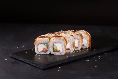 Somon avacado cucmber cheam peyniri nori susam ve siyah arka planda teriyaki ile birlikte yılan balığı suşisi rulosu. Yatay fotoğraf. Kanada yuvarlanıyor.