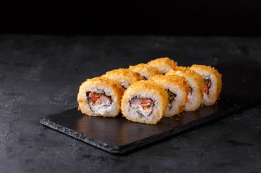 Suşi, somon, yılan balığı, karides, nori, krem peynir, siyah arka planda salatalık. Yatay fotoğraf. Alçak tuş.