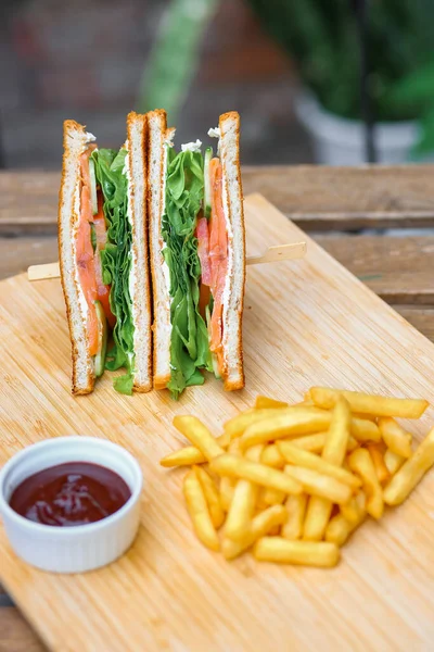 Somonlu sandviç, salata, sebze, marul, domates, soğan ve ahşap zemin üzerinde taze dilimlenmiş ekmek. Dikey fotoğraf. Kapat.