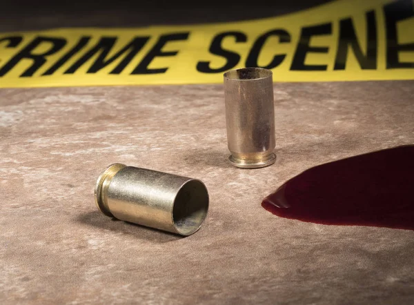 Police tape behind with empty pistol brass and blood in the fore — Stock Photo, Image