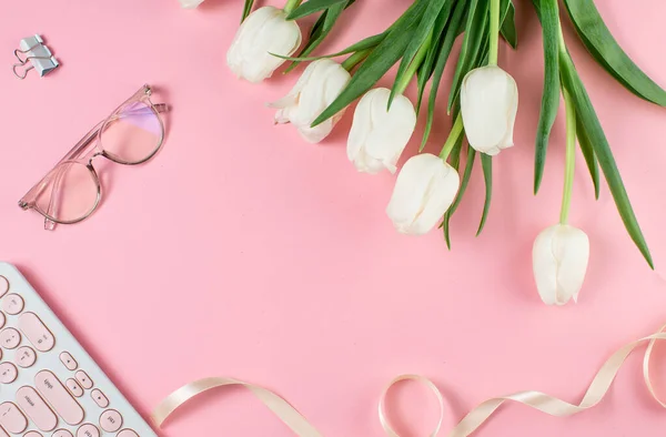 İş kadını konsepti. Pembe arka planda dizüstü beyaz laleler ve gözlük..