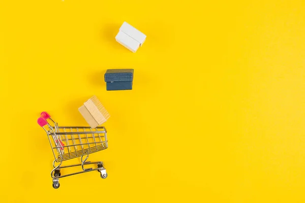 Alışveriş konsepti. Sarı arka planda izole edilmiş hediye arabaları ve paketler..