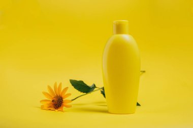 Vücut bakımı ürünü ve sarı arka planda bir çiçek.