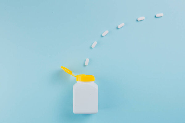 Таблетки разбросаны по бутылке на голубом фоне
