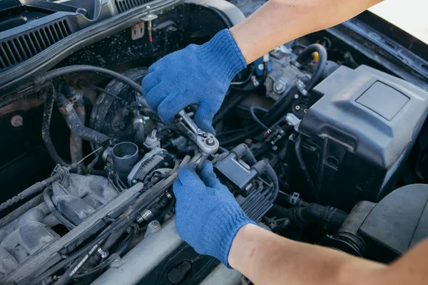 Mavi eldivenli bir tamirci araba motorunu tamir ediyor.