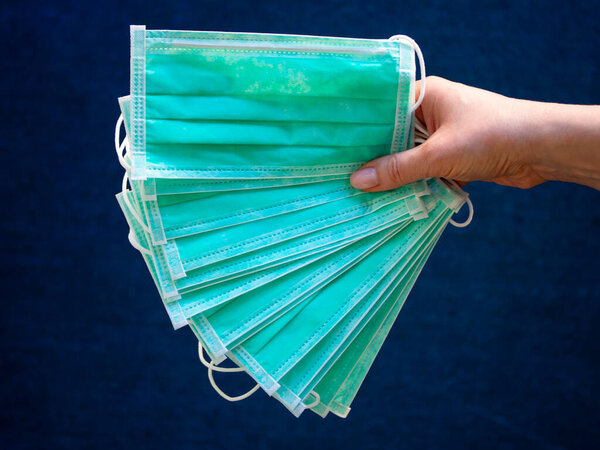 Close-up of medical or surgical green color masks in the hand of a young woman on a dark blue carpet textile background. The concept of medical supplies or accessories for personal protection.