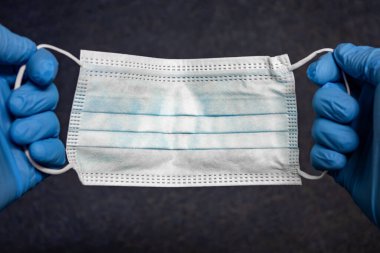 Tıbbi ya da cerrahi açık mavi maske yakın plan elinde koyu renkli halı tekstil arka planında mavi eldivenlerle. Kişisel koruma için tıbbi malzeme veya aksesuar kavramı.