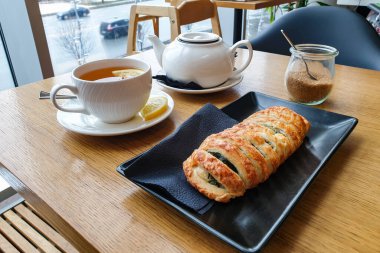 Sarı limonlu ve kurabiyeli bir fincan siyah çay ya da siyah tabakta turta. Beyaz çaydanlığın yanında ve bir kutu şeker. Pencereden perdeye doğru bahar ışığı parlıyor..