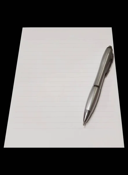 Close-up of a notepad. Gray silver ballpoint pen on the sheet. Notepad with lines. Isolated on black background. Top view of blank note paper with pen. Copy space. School and education concept.