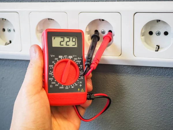 Elindeki çoklu metreyi kullanarak prizdeki elektriği ölçmek. LCD ekranlı kırmızı cep dijital multimetresi. Prizde test ipuçları var. Yüksek kalite yakın çekim fotoğrafçılık.