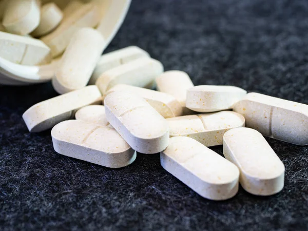 Tepetaklak olmuş ilaç kavanozundan dökülen beyaz bitkisel opioid haplarının yakın plan çekimi. Gri mikrofiber yüzeyde beyaz oval tabletler. Kopya alanı ile tıp konsepti teması arkaplanı.