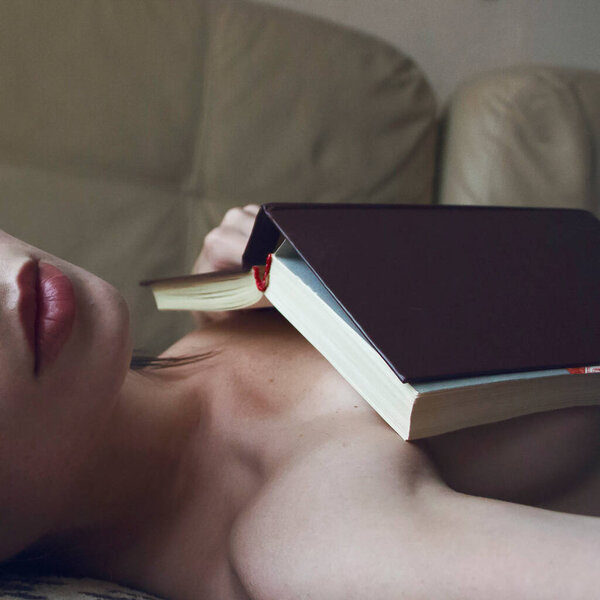 Girl lies on the bed and hides behind a book