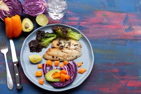 Fish with vegetables, purple cabbage, red bell pepper, shadow on a blue background, for summer